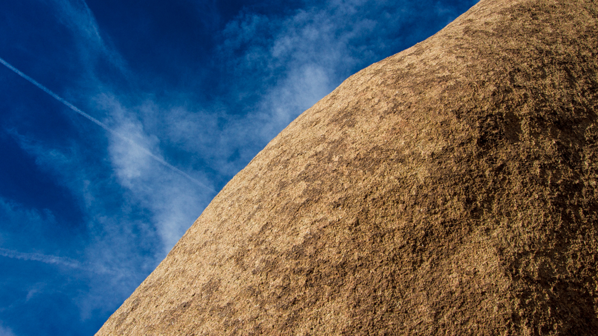 a bright blue sky, contrasting a low angled granite rock face