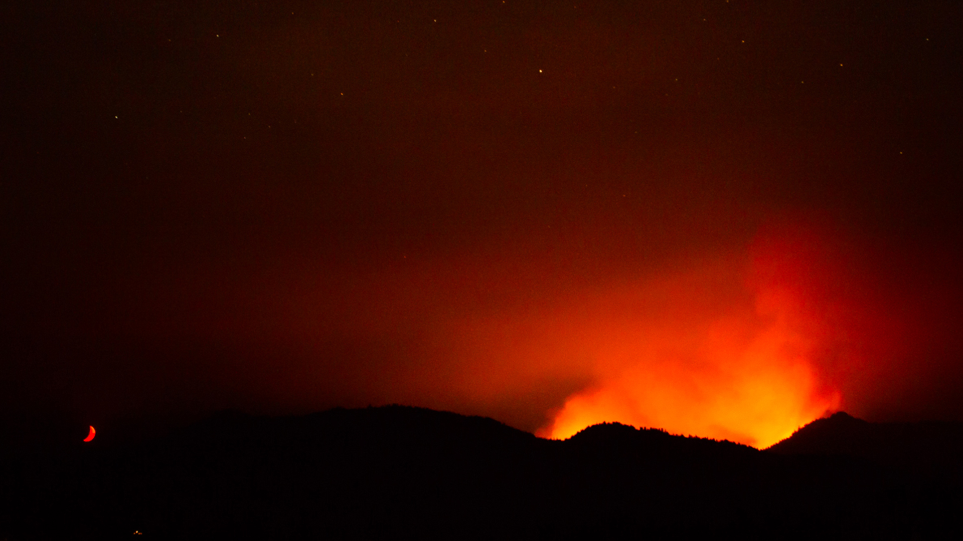 a forest fire at night, long exposure, the moon glows red like the smoke